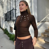 Woman wearing a brown turtleneck sweater with decorative buttons in front of a building.